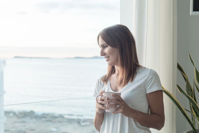 Woman enjoying the view out window while holding cup of coffee