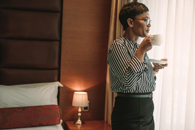 Woman in business wear standing in hotel room and having a cup of coffee