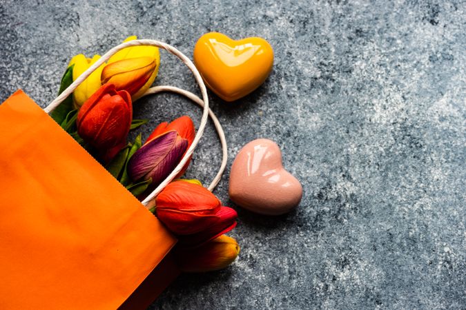 Pink and orange heart ornaments on grey counter with bag of fresh tulips
