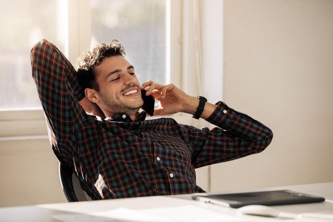 Entrepreneur relaxing back on his chair and talking on cell phone sitting at his desk