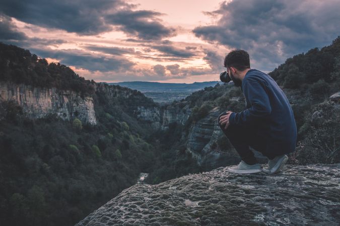 man with photo camera sitting on hill mountain with magnificent sunset