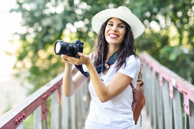 Smiling woman walking with SLR camera, wearing straw hat outside