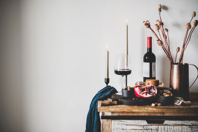 Rustic setting of wine, cheese, long candles, with pomegranate, and dried poppies, with copy space