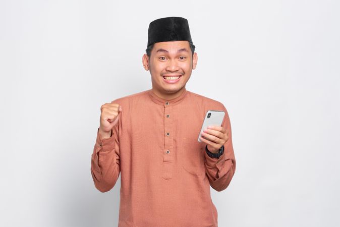 Happy Muslim man in kufi hat holding mobile phone