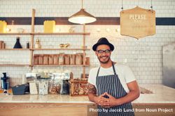 Portrait of happy young man wearing an apron and hat leaning to a cafe counter 4ZeGW5