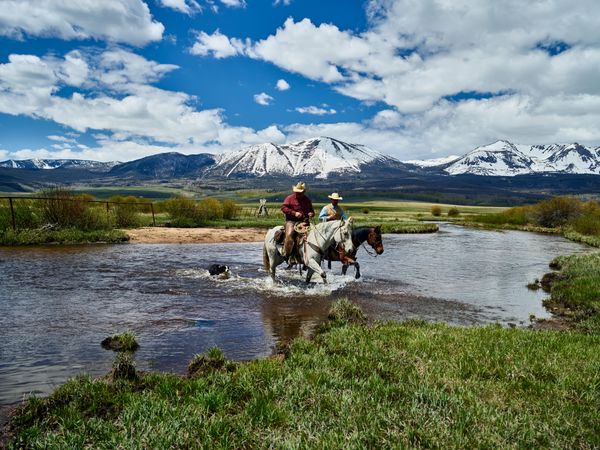 Two cowboys fording river on horseback in Colorado