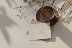 Cup of coffee and checkered plaid on table with blank card and shadow