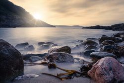 Landscape of rocked seashore with rising sun on cloudy sky