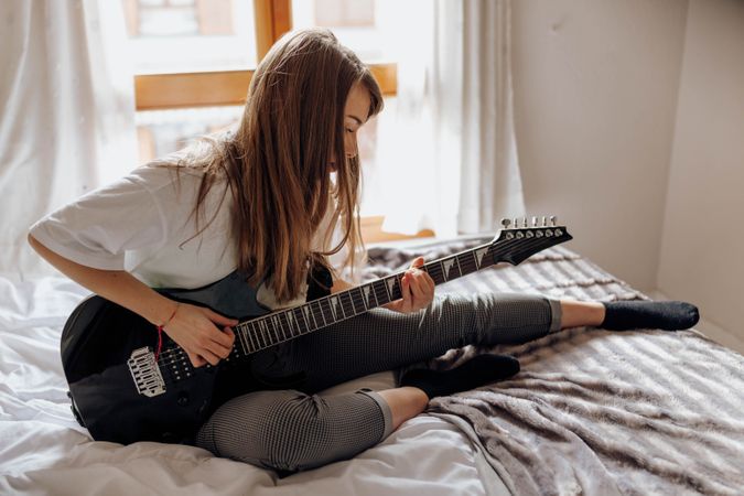 Young brunette woman playing guitar on bed