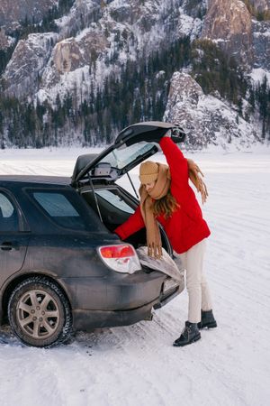 Female traveler standing in snowy valley and opening car trunk