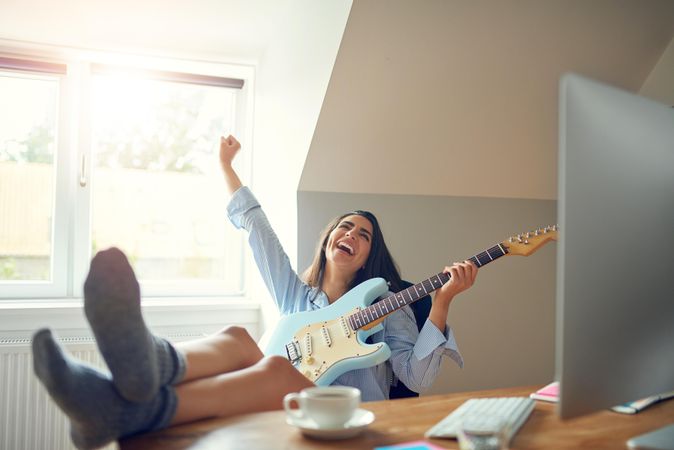 Happy female playing guitar at her desk