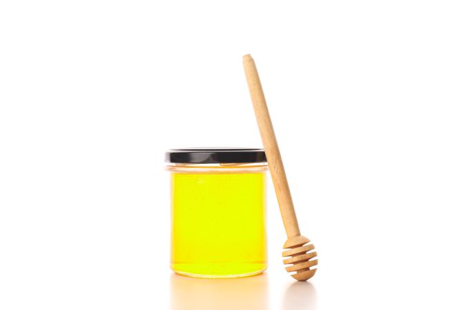 Glass jar with honey and dipper isolated on plain background
