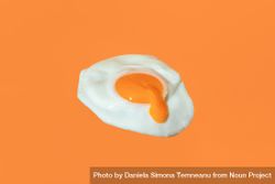 Fried egg minimalist on an orange background with egg yolk dripping 5lzjmb