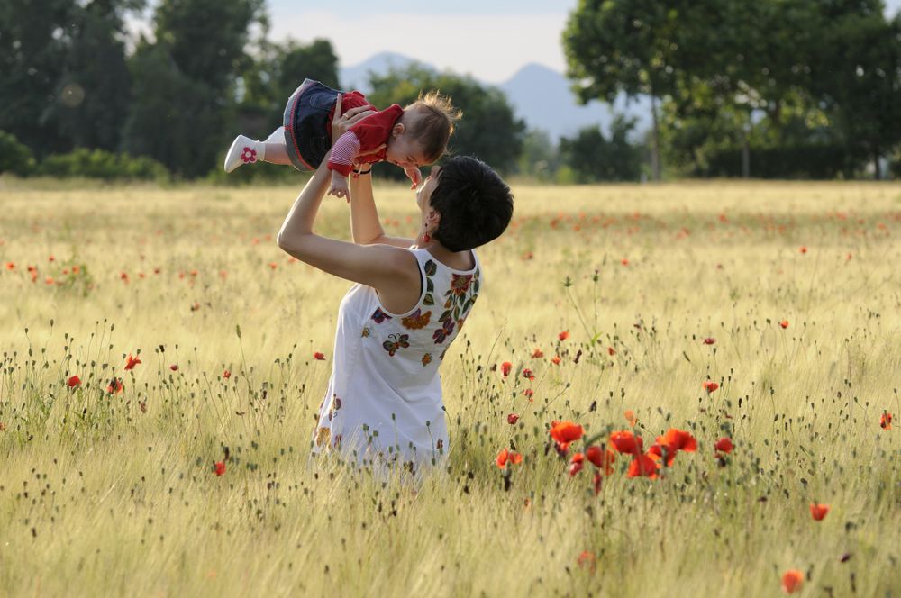 Mother holding up little girl in poppy field