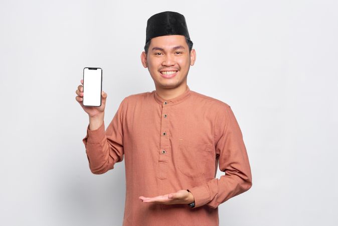 Happy Muslim man in kufi hat presenting mobile phone with black screen