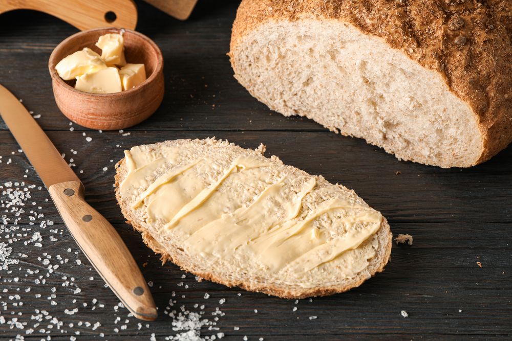 Cutting boards, bread, salt, knife and butter on wooden background, closeup