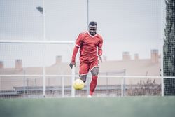 Black soccer player with red outfit playing soccer.