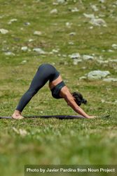 Woman in a grass field doing downward dog yoga pose 4mWne0