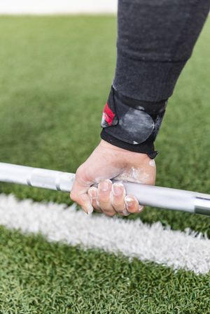Man hand in chalk holding barbell on sports ground