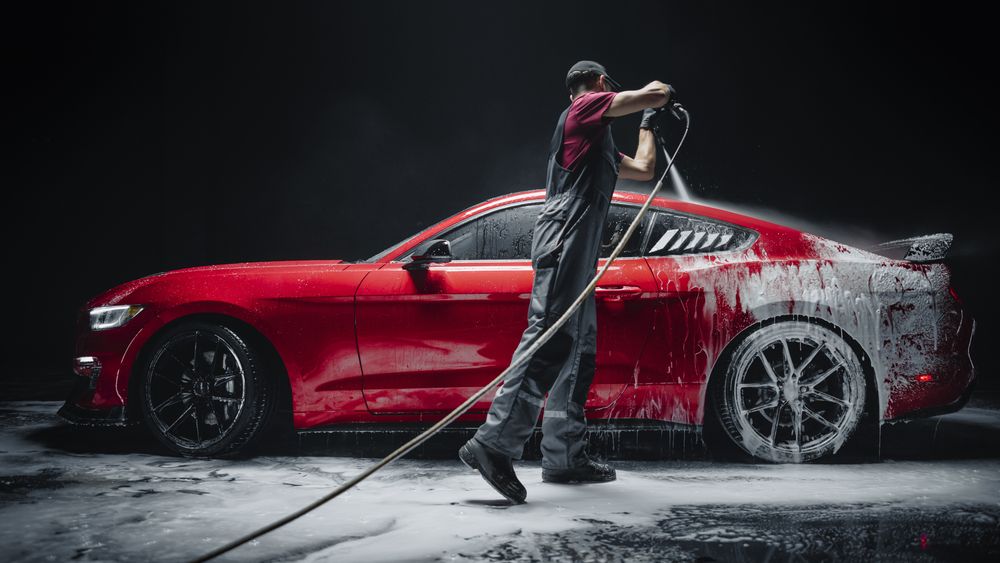 Car Wash Specialist Using Pressure Washer to Rinse a Red Modern Sportscar.