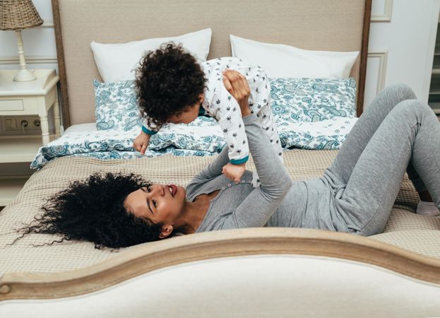 Mother lying on bed holding her toddler above her head