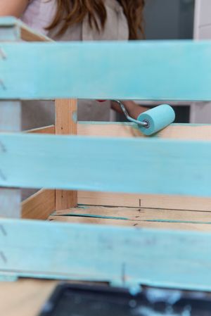 Woman paining wooden box in blue color with roller