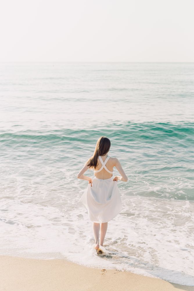 Back view of woman in light dress standing on beach