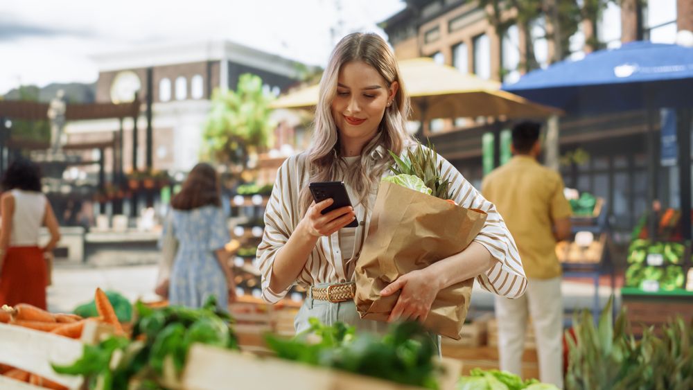 Female Customer Using Smartphone, Checking a List of Ingredients Online and Checking Social Network for Delicious Dinner Recipes.