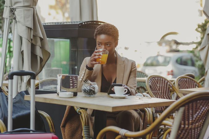 Smiling Black woman with smartphone sitting at table near luggage in cafe