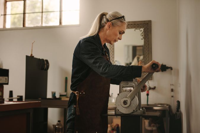 Mature woman goldsmith crafting metal on craft rolling machine