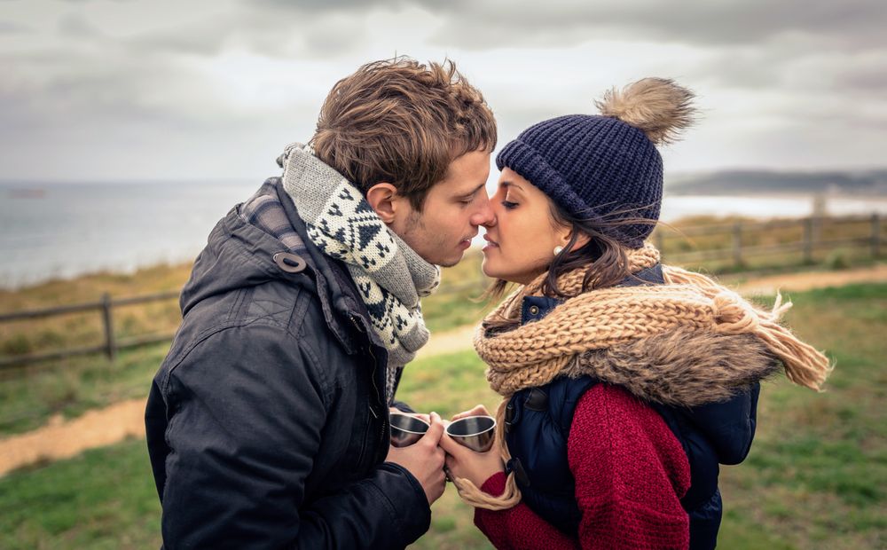 Couple kissing with coffee mugs on cliff above the ocean