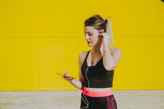 Woman with earphones running near wall