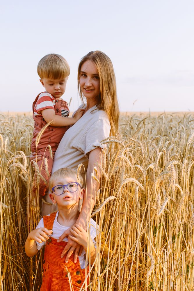 Young mother with little sons standing on wheat field in countryside