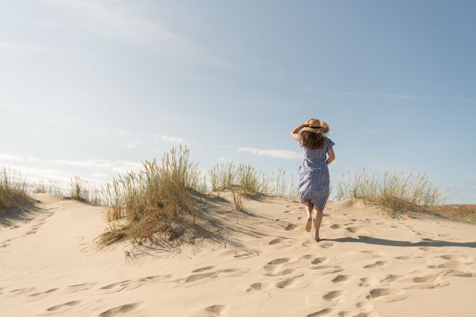 adult woman in casual dress and straw hat walking having good time on sand dune
