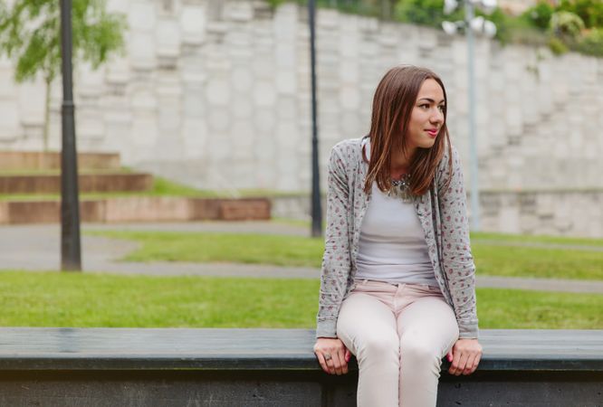 Young woman sitting outside on park bench smiling at camera
