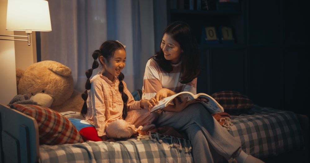 Korean Mother Reading a Fairytale to Her Lovely Small Daughter in Bed Before Going to Sleep.