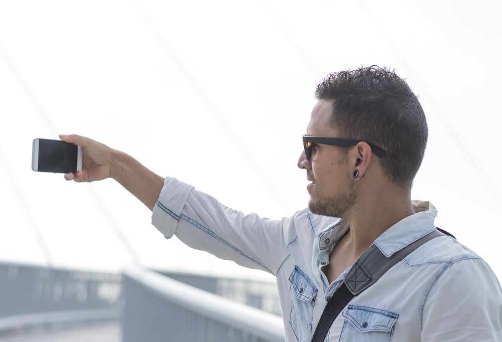 Male in denim shirt standing outside taking photo with phone