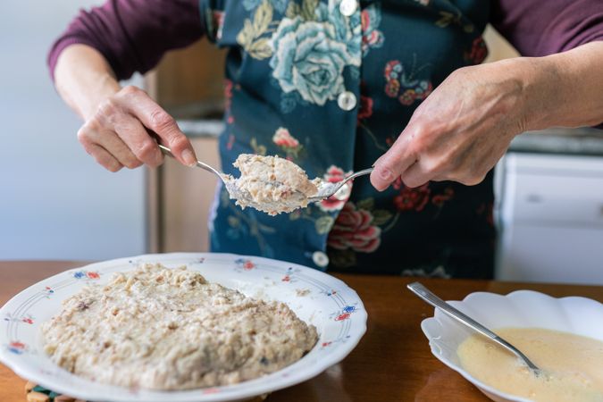 Older woman coating the croquette dough with flour and egg