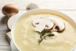 Close up of bowl of creamy mushroom soup on napkin on wooden table