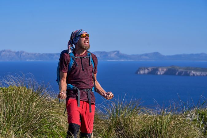 Male traveler standing on cliff and celebrating achievement