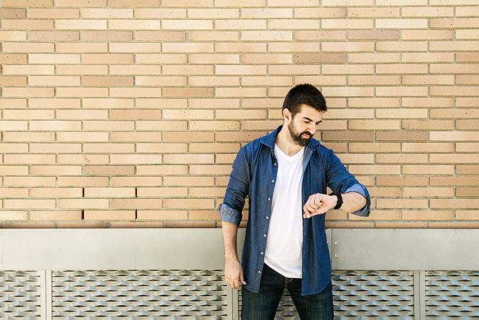 Man checking watch in front of brick wall