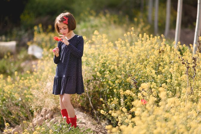 Girl smelling a flower in a beautiful field surrounded by yellow flowers