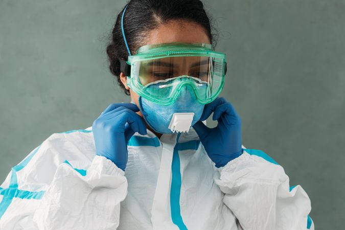 Female doctor in PPE gear and medical hazmat suit adjusting her mask