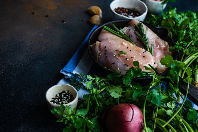 Raw chicken with rosemary sprig on kitchen slab with seasoning and copy space