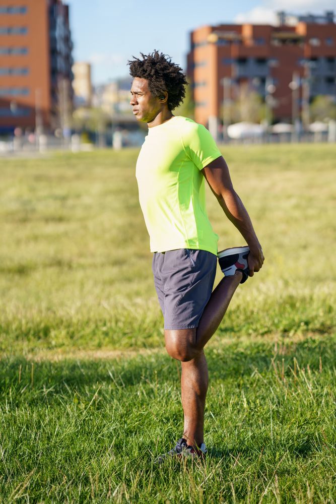 Man stretching quads behind him at park