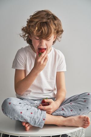 Boy in sleepwear biting delicious strawberries at home