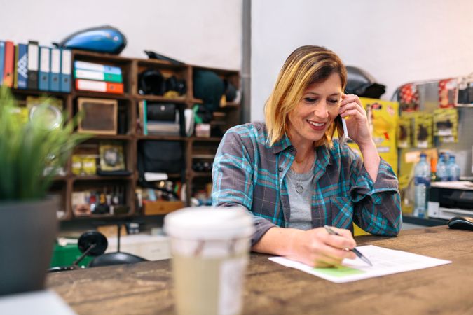 Portrait of smiling blonde young woman receiving order by phone for ecommerce shop