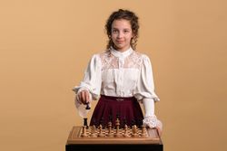 Young girl in vintage lace blouse playing chess thoughtfully.