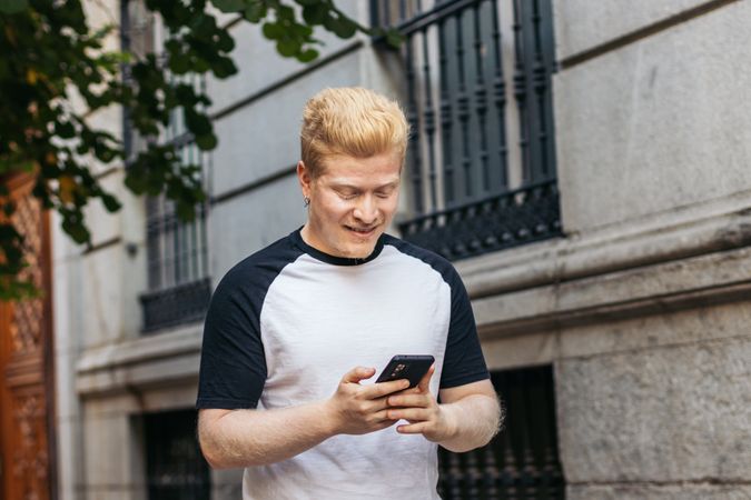 Latino man with albinism using smartphone while walking in the city