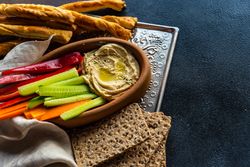 Creamy hummus dish served with chopped veggies, rye crackers and bread sticks on trey